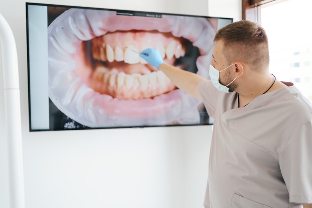 dentist-in-medical-mask-pointing-on-the-patient-teeth-on-a-big-screen-explaining-treatment-phases_158595-7729.jpg